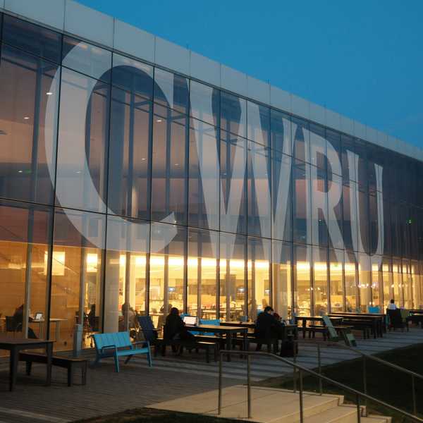 Large "CWRU" lettering on the side of Tinkham Veale University Center glows at dusk as students study inside.